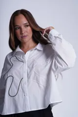 Camisa negra de manga larga con cuello clásico y cierre frontal con botones. Presenta bordados abstractos en blanco y negro en el frente.