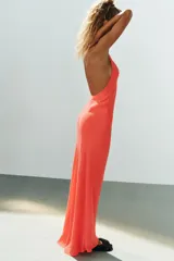 Vestido largo color salmón con cuello halter, escote redondo y espalda descubierta. Cuenta con bajo acabado asimétrico, cierre en el cuello con botón y cremallera oculta en la espalda.