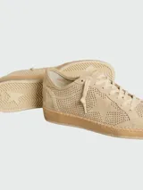 Championes Golden Goose modelo Ball Star, confeccionados en gamuza color beige con diseño perforado en toda la superficie. Presentan una estrella lateral característica, cordones al tono y una suela de goma con costuras visibles.