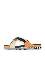 Sandalias Kenner Rakka Cross Craft con tiras cruzadas de tela color beige y ajuste con hebilla de plástico negra. Suela de goma negra con detalles en naranja y verde.