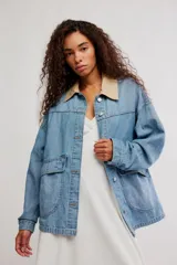 Campera de denim oversize color celeste, con hombro caído, cuello de lona beige en contraste, bolsillos frontales asimétricos, cierre frontal con botones y puños abotonados.
