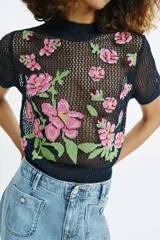 Top de punto calado color azul marino, con cuello subido y manga corta. Presenta un diseño con flores bordadas en tonos rosados y verdes en la parte delantera.