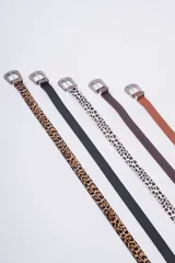 Cinturón de estilo western con hebilla metálica plateada ornamentada. Disponible en varios colores y estampados: cuero marrón claro, cuero marrón oscuro, estampado dálmata (blanco y negro) y cuero negro liso. También disponible en estampado leopardo.