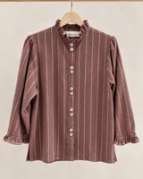 Camisa de algodón color bordó con diseño de rayas verticales blancas, cuello alto con volados, mangas largas con puños fruncidos y cierre frontal con botones claros.