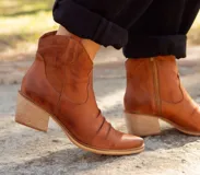 Botineta estilo texana de caña baja, color terracota, confeccionada en cuero natural con acabado arrugado en la parte frontal. Presenta taco cuadrado de madera y cierre lateral.