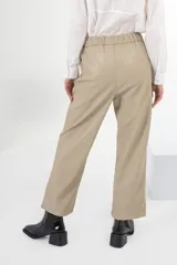 Pantalón de vestir color beige, de corte recto, con bolsillos laterales y traseros. Se ajusta a la cintura con cinturón de cuero marrón.