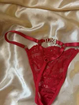 Tanga de hilo roja con diseño de tiras finas, argollas metálicas y detalle de la palabra 'Tuya' en strass en la parte trasera.