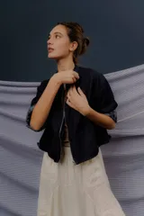 Campera de denim azul oscuro, de corte corto y estilo bomber, con cierre frontal y detalles de forrería a cuadros visibles en el interior de los puños.