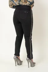 Pantalón de jean negro alicrado, modelo calza sin cierre, con faja en la cintura y aplique de galón bordado en los costados.