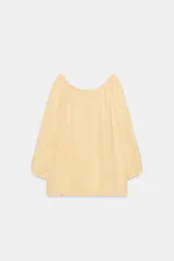 Blusa de lino color amarillo pastel, con escote recto ajustable mediante lazadas, hombros descubiertos y mangas largas abullonadas con puños elásticos.
