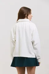 Buzo de algodón con diseño bicolor en blanco y verde inglés, cuello tipo chomba con botones frontales, mangas largas con puños y corte holgado a la cintura.