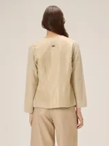 Saco de punto color beige con acabado metalizado, manga larga, cuello redondo y cierre frontal con botones. El diseño combina frente y mangas de tejido abierto con espalda en tela de lino.