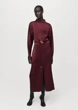 Vestido midi de tejido satinado color bordó, con cuello alto, mangas largas, diseño recto y abertura frontal en el bajo. Incluye un cinturón ajustable delgado con hebilla dorada.