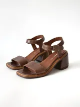 Sandalias de cuero color chocolate, con taco cuadrado de 6 cm, tira ancha en la parte delantera y tira en el tobillo con hebilla metálica ajustable.