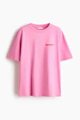 Remera oversized de punto de algodón color rosado, con hombros caídos, cuello redondo y pequeño texto estampado en el pecho.