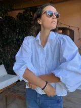 Camisa blanca de corte holgado con mangas abullonadas y puños elásticos. Presenta cuello clásico y cierre frontal con botones.