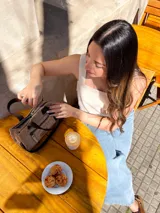 Cartera tipo tote de cuero color beige, con doble asa corta marrón y cierre superior con cremallera. Tiene un bolsillo frontal con cremallera y forro interior de tela con un bolsillo.