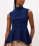 Blusa azul marino sin mangas de la marca Cortelle, con cuello alto, recortes estructurales y dobladillo estilo peplum asimétrico.