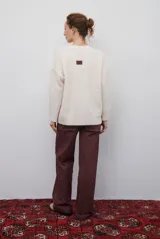 Buzo de punto color beige con diseño de trenzas y costuras decorativas en contraste que forman rombos. Presenta cuello redondo, mangas largas y puños acanalados.
