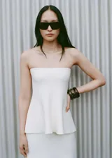 Top bandeau blanco de punto fino con corte peplum. Diseño sin breteles, ideal para fiestas y ceremonias.