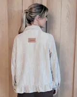 Sobrecamisa de pana color marrón oscuro, con cuello camisero, cierre frontal de botones y detalle de volado en el ruedo. Presenta mangas largas con puños y bolsillos frontales aplicados.