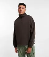Buzo de corte holgado tipo ballon, color marrón oscuro, con cuello alto y cierre frontal parcial. Presenta mangas largas con puños elásticos y cordón ajustable en el ruedo.