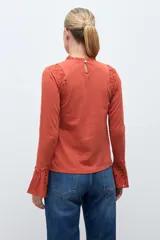 Remera de manga larga color terracota, con cuello alto y detalles de broderie en los hombros y puños acampanados.