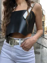 Top corto de ecocuero negro con corte asimétrico y un tirante ancho de ecocuero blanco con textura de piel de cocodrilo. Se ajusta con botones o lazo en la espalda.