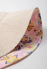 Gorro tipo bucket hat estampado con flores y hojas en tonos verde y celeste sobre fondo blanco. Es reversible.