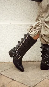 Bota de cuero color negro, de caña media, con punta fina y múltiples hebillas metálicas plateadas.