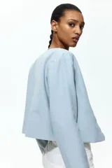 Chaqueta celeste de manga larga, con cuello redondo y frente abierto con bordes festoneados.