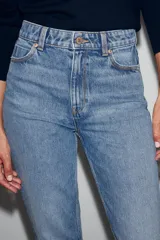 Jeans mom fit de tiro alto y diseño tobillero, confeccionados en denim de lavado medio con cinco bolsillos, trabillas para cinturón y cierre frontal con cremallera y botón metálico.