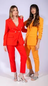 Blazer cruzado de color naranja vibrante, con solapas anchas y botones plateados. Presenta un cinturón a juego que ajusta la cintura y bolsillos frontales con solapa.