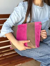 Cartera tipo sobre de cuero con diseño de rayas verticales en tonos verde menta y marrón tostado. Cuenta con detalles de borlas colgantes en los laterales.