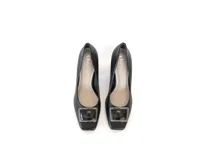Zapatos de tacón de cuero negro, con punta cuadrada, aplique metálico en el empeine y tacón ancho de altura media con textura geométrica.