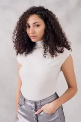 Top sin mangas, cuello tortuga, color blanco con acabado brillante o metálico. Tejido acanalado y ajustado al cuerpo.