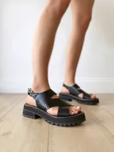 Sandalias negras de cuero con tiras cruzadas, plataforma track y hebilla lateral.