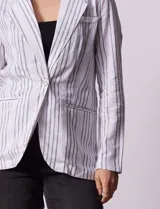 Blazer blanco con rayas verticales negras, cuello con solapa, abertura central con botón y bolsillos delanteros.