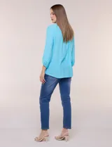 Blusa celeste de silueta suelta y textura liviana, con escote en V, cuello mao y cierre frontal de botones. Cuenta con alforzas verticales en el pecho y mangas tres cuartos con puños elastizados y detalle de galón calado.