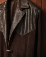 Blazer de diseño estilo western confeccionado en una combinación de cuero con efecto envejecido y gamuza color chocolate. Cuenta con solapas clásicas y cierre frontal con botón tipo duffel.