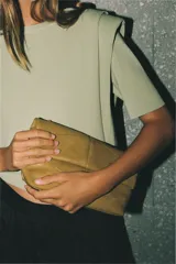 Bolso de mano tipo sobre color mostaza, con diseño acolchado y costuras geométricas. Cuenta con cierre imantado y asa tipo bandolera extraíble.