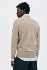 Remera polo de manga larga en punto fino color beige, con cuello clásico y tapeta de dos botones. Presenta remates acanalados en puños y bajo.