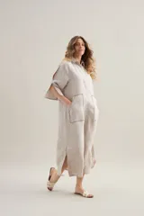 Vestido largo de lino color beige, de silueta relajada, con cuello camisero, mangas cortas con aberturas, bolsillos delanteros amplios con detalles de costura a contratono y aberturas laterales en el ruedo.