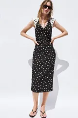 Vestido midi de lunares, color negro con lunares blancos, escote en V y mangas sisa con hombreras. Presenta frunces laterales en la cintura y cierre en la espalda con cremallera oculta.