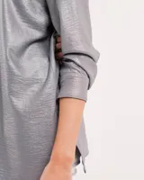 Camisa oversized con terminación metalizada color gris plomo. Tiene botones a tono en el delantero, largo por debajo de la cadera y tajos a los costados.