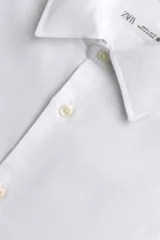 Camisa blanca de manga larga con cuello italiano y puños abotonados, confeccionada en tejido de algodón.