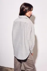 Camisa oversize color arena con rayas verticales marrones, de manga larga y cuello clásico.