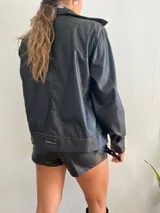 Campera negra de cuero sintético con costuras blancas a contraste, cierre con botones metálicos y cuello clásico.