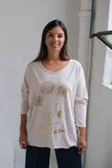 Remera de corte holgado y mangas largas, color beige, con estampado floral en tonos dorados en la parte frontal.