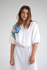 Vestido camisero corto color amarillo pálido con estampado floral en el hombro izquierdo y cinturón de tela con diseño geométrico.